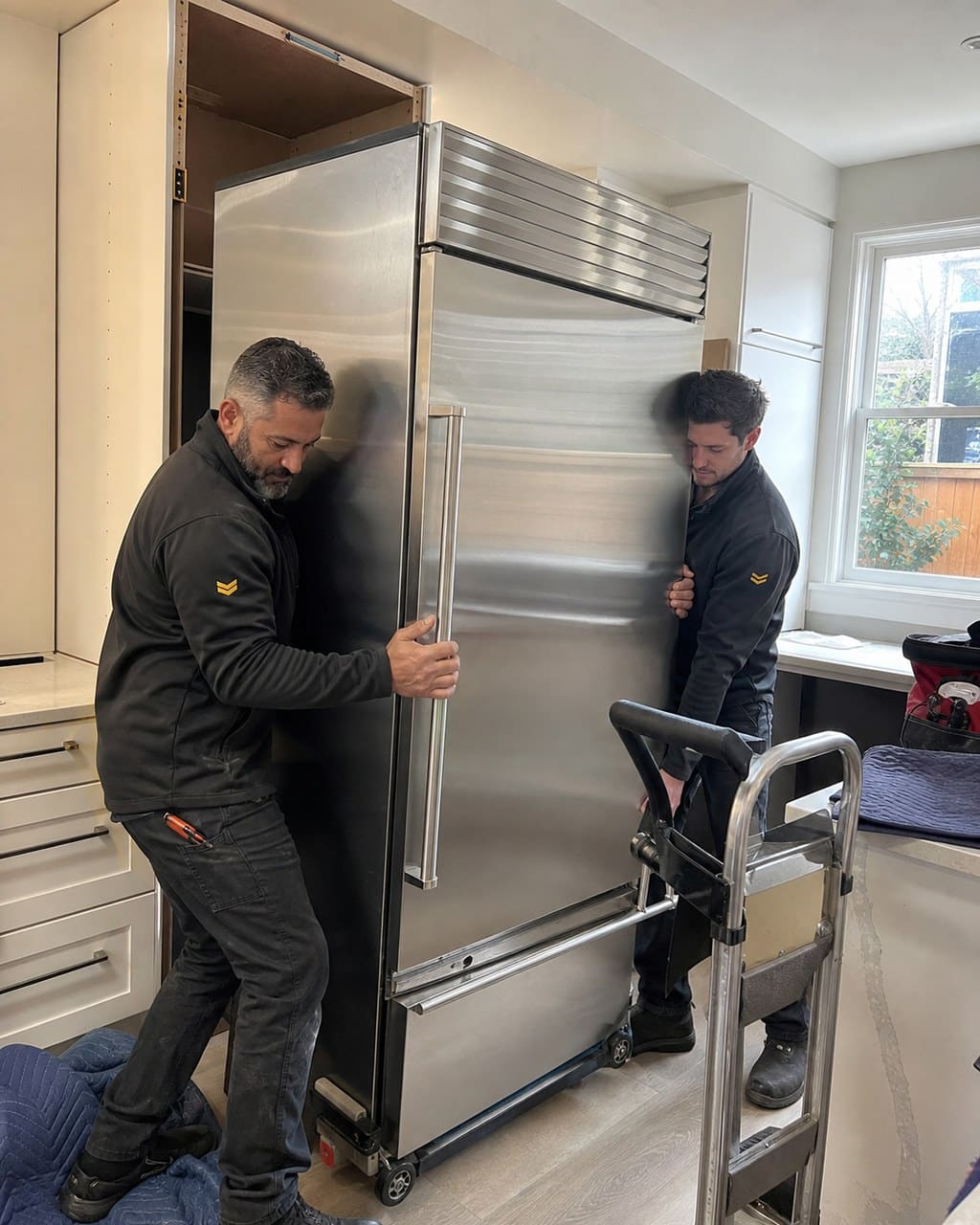 Two Sub-Zero Fremont technicians sliding a built-in refrigerator out for service